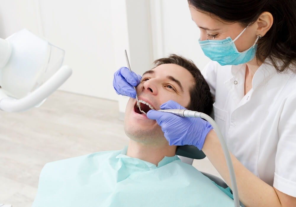 A man sits in a dental chair while a dentist cleans his teeth